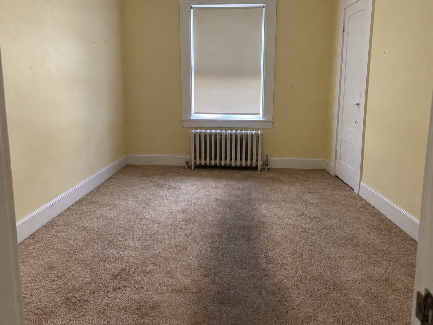 Empty room after a hoarding cleanout, with the original worn carpet and radiator retained.