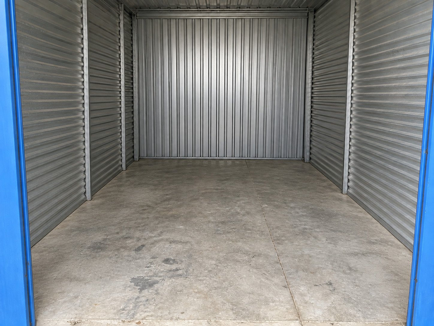 Storage unit empty after contents removal, with its worn concrete floor retained.