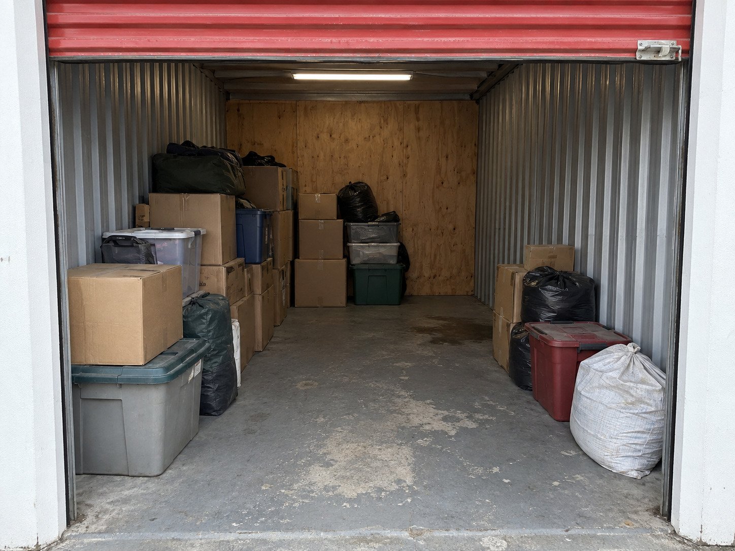 Cartons, totes and bags in a worn storage locker before contents removal.