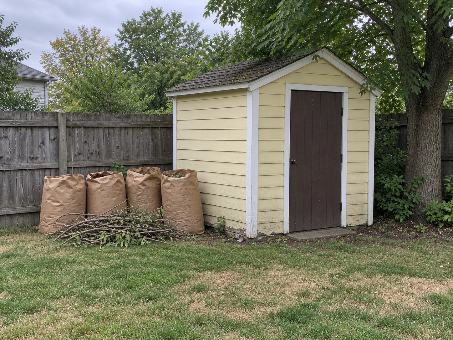 Yard-waste bags and pruned branches beside a shed before pickup.