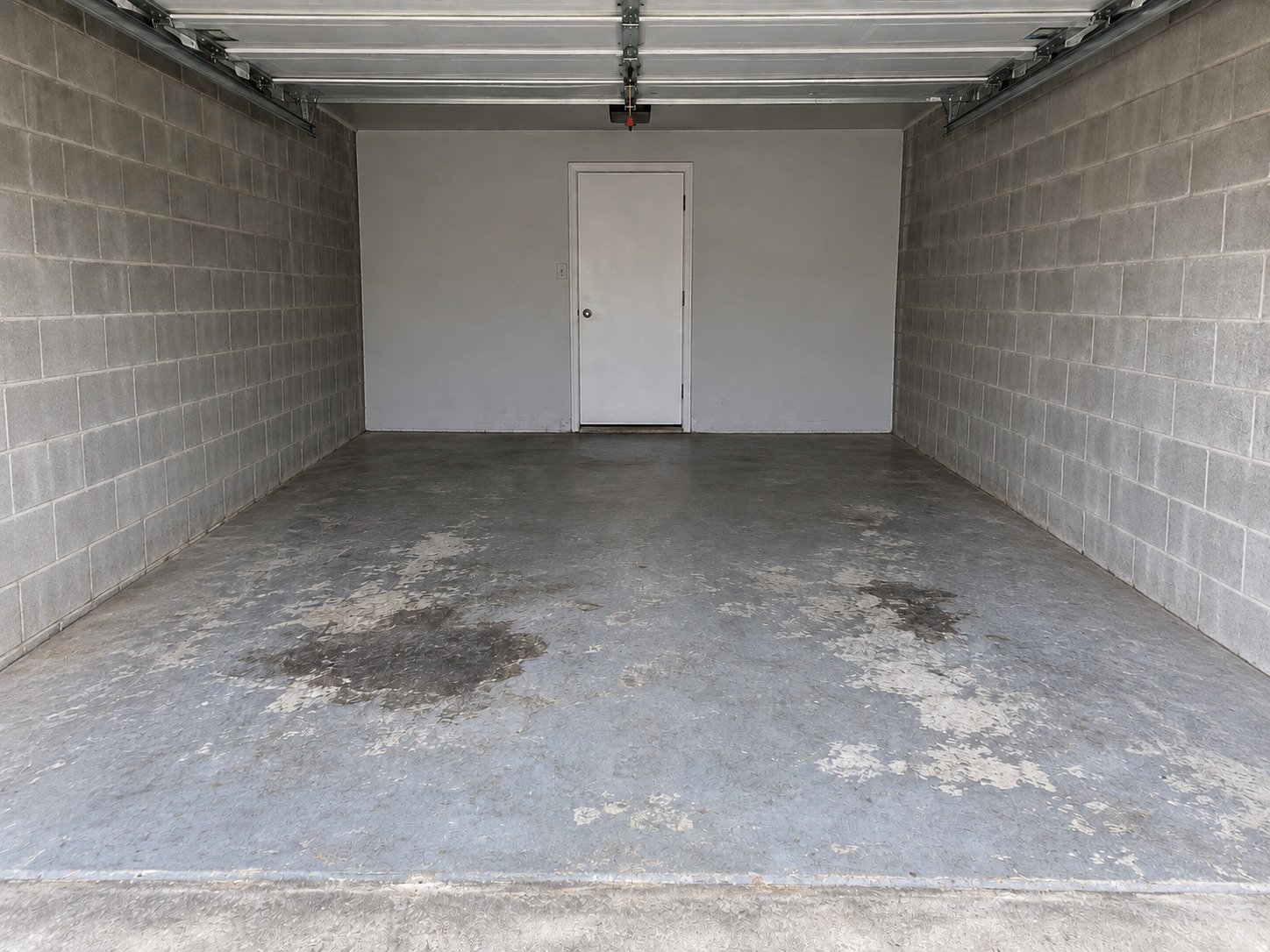 Empty garage after contents removal, with original floor wear and stains retained.