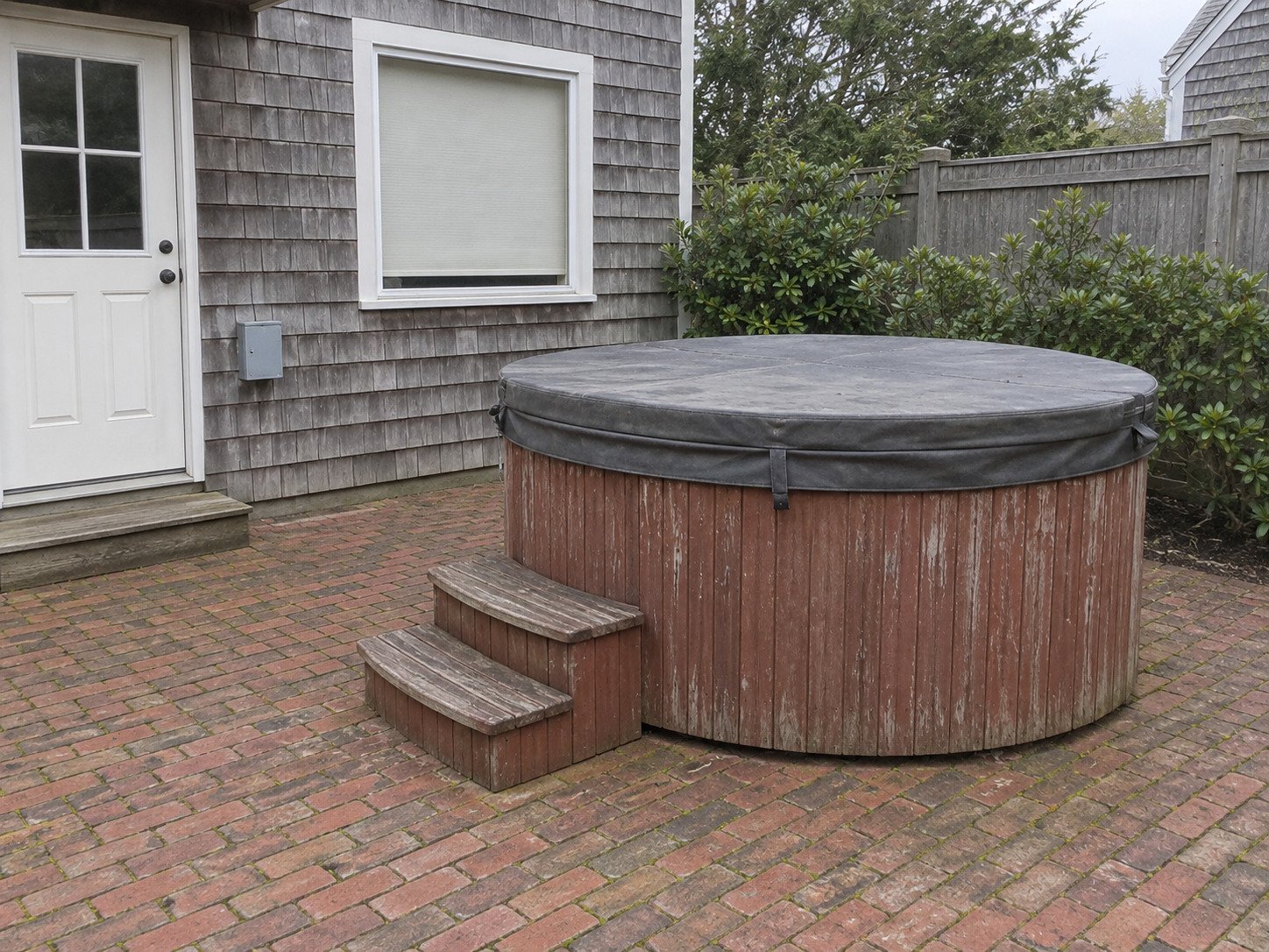 Old round hot tub on a brick patio before removal.