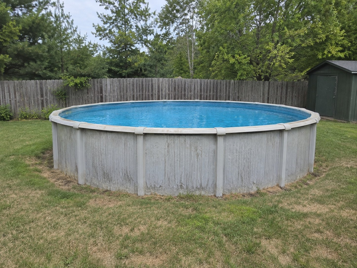 Weathered above-ground pool in a fenced backyard before removal.