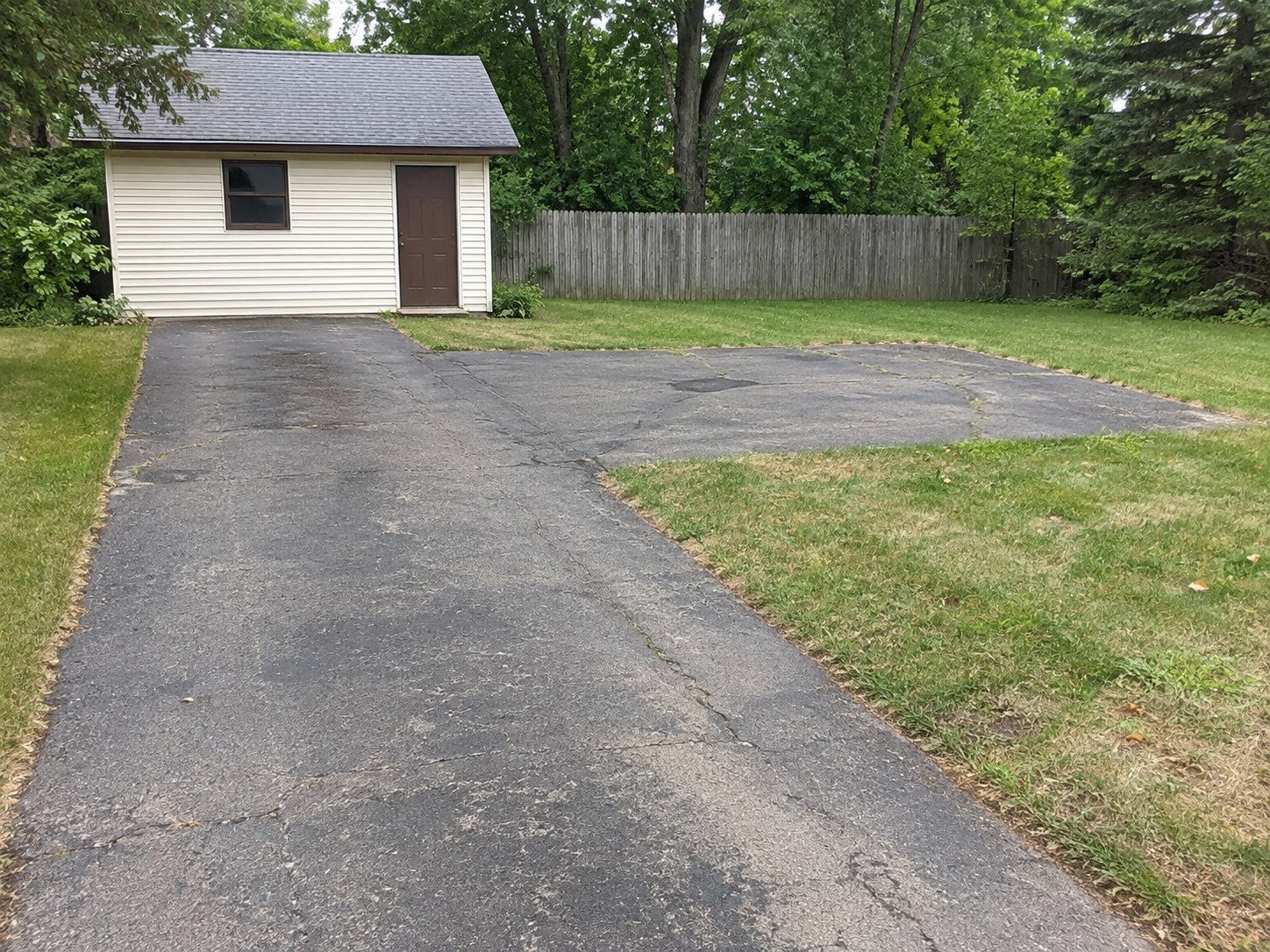 Old asphalt parking spur beside a utility building before removal.