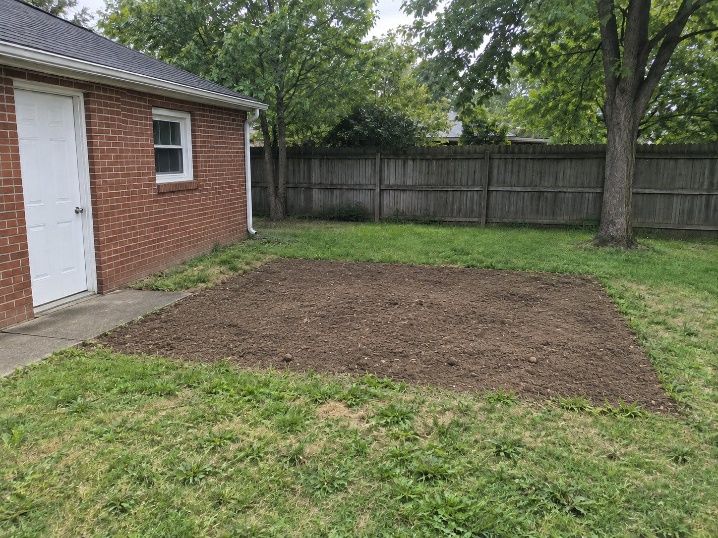 Rectangular soil footprint after concrete patio removal, with the garage access walk retained.