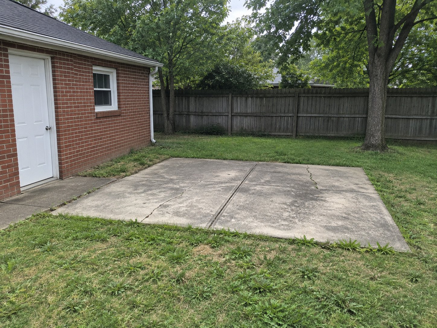 Old cracked concrete patio beside a brick garage before removal.