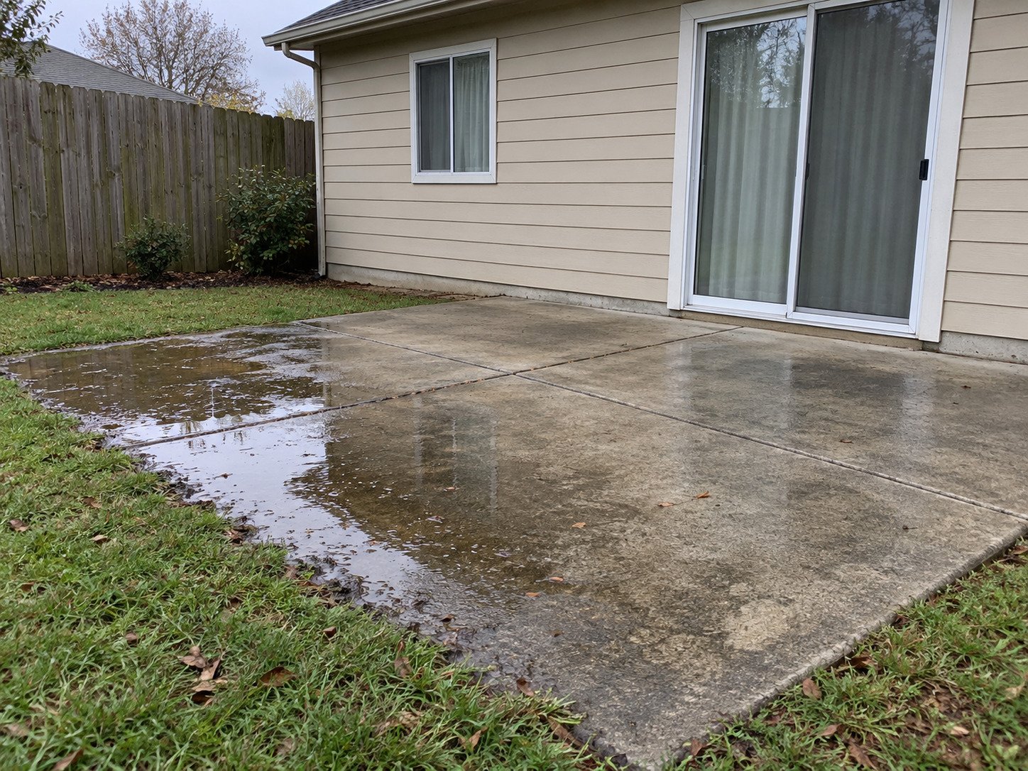 Patio with standing rainwater along the lawn edge before drainage improvement.