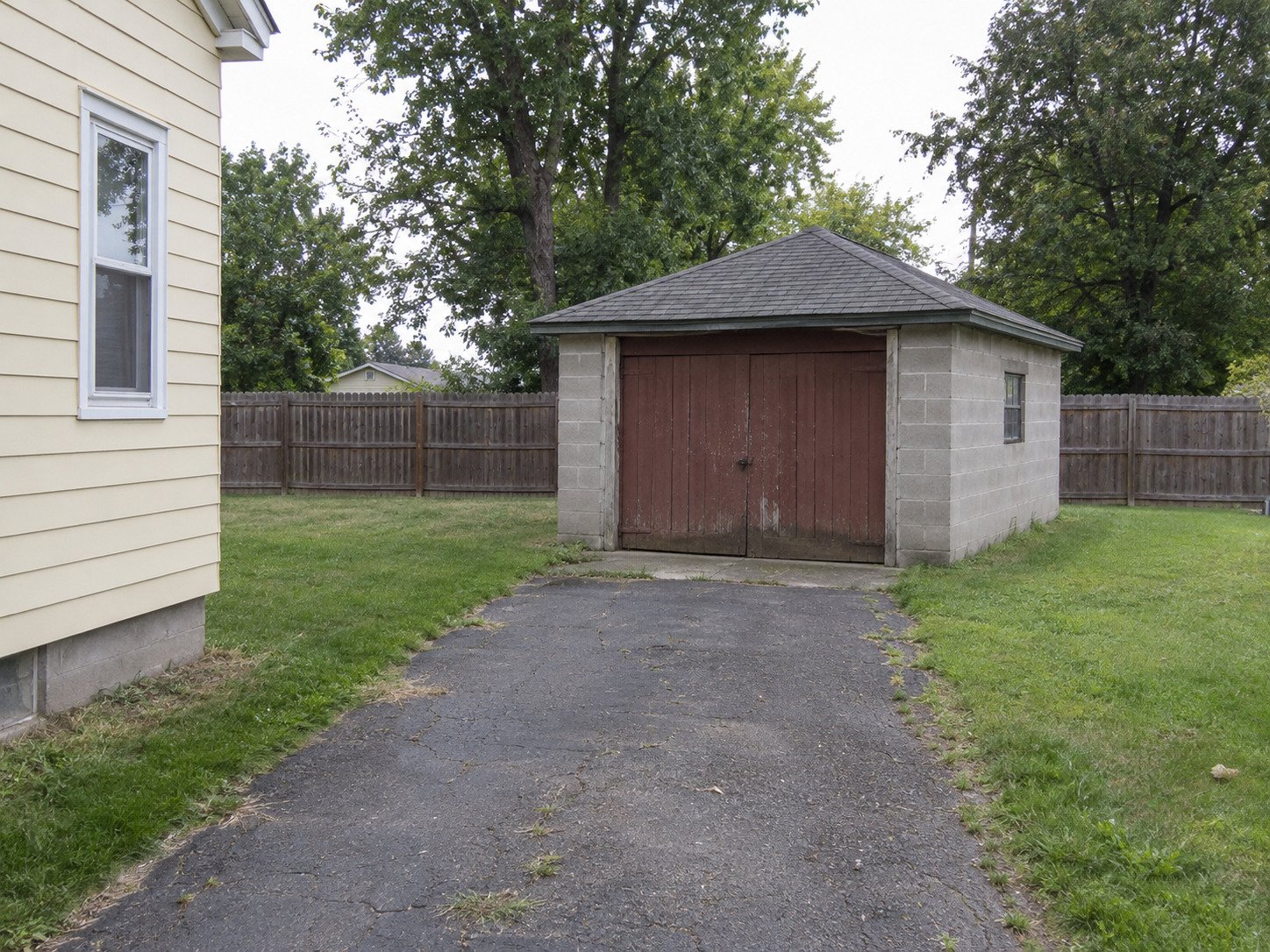 Old detached block garage beside a worn driveway before demolition.