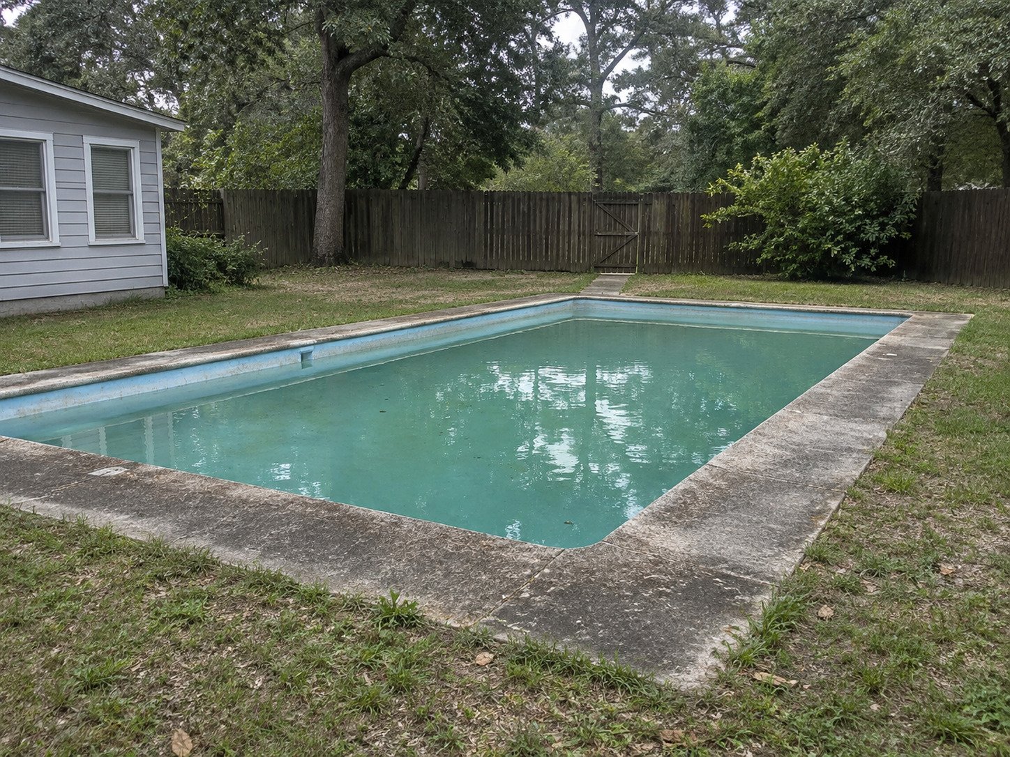 Aging rectangular inground pool in a fenced backyard before removal.