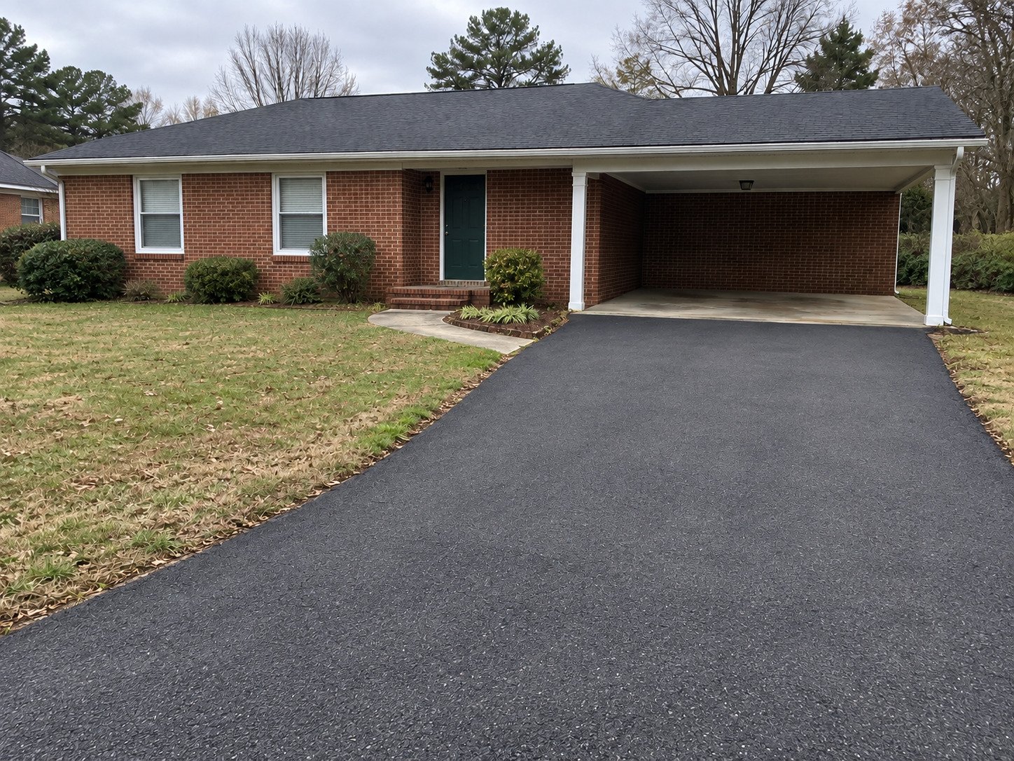 Same carport driveway after replacement with compacted asphalt, with house and landscaping unchanged.