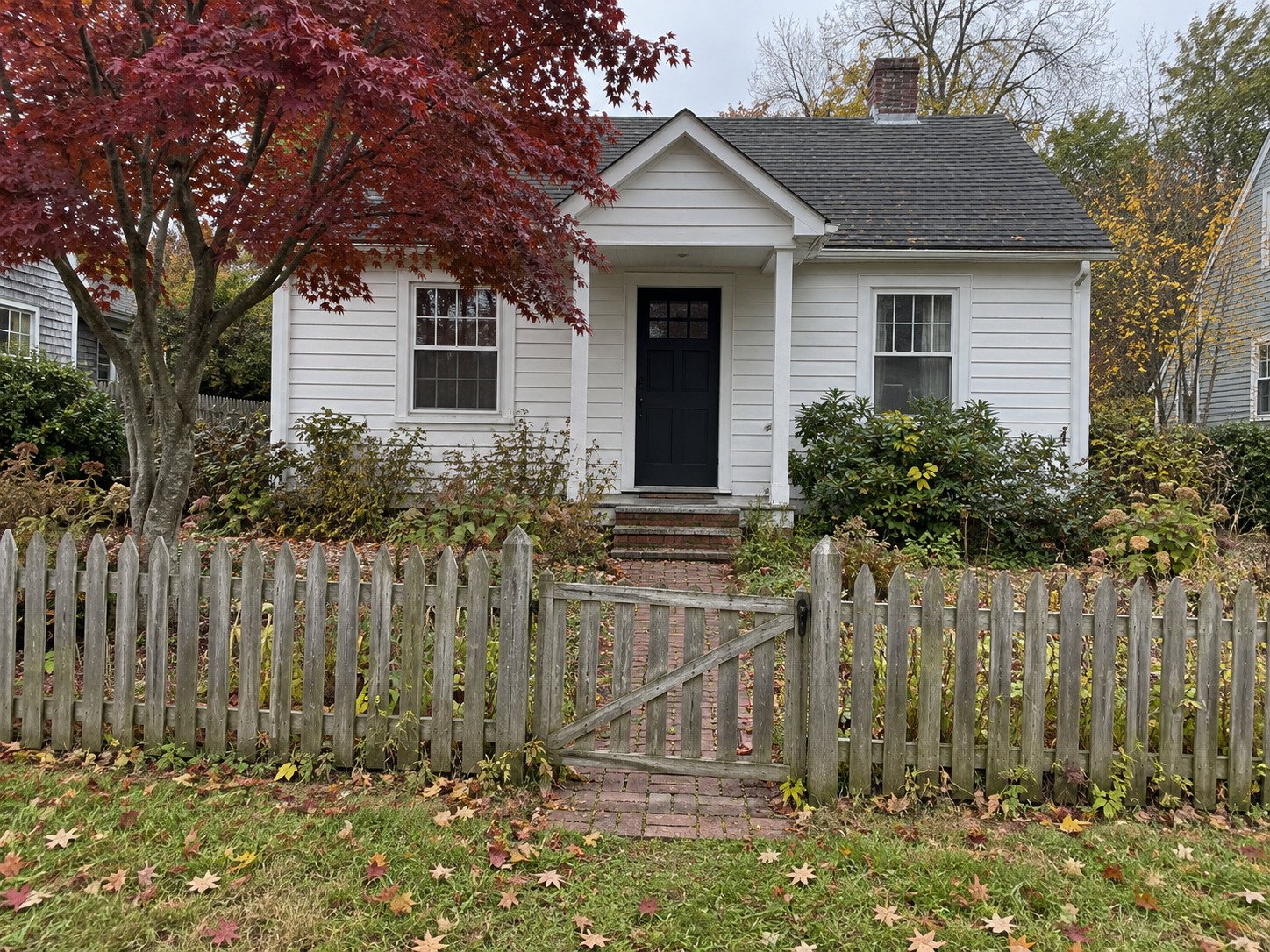 Weathered picket fence and sagging gate outside a small white cottage.