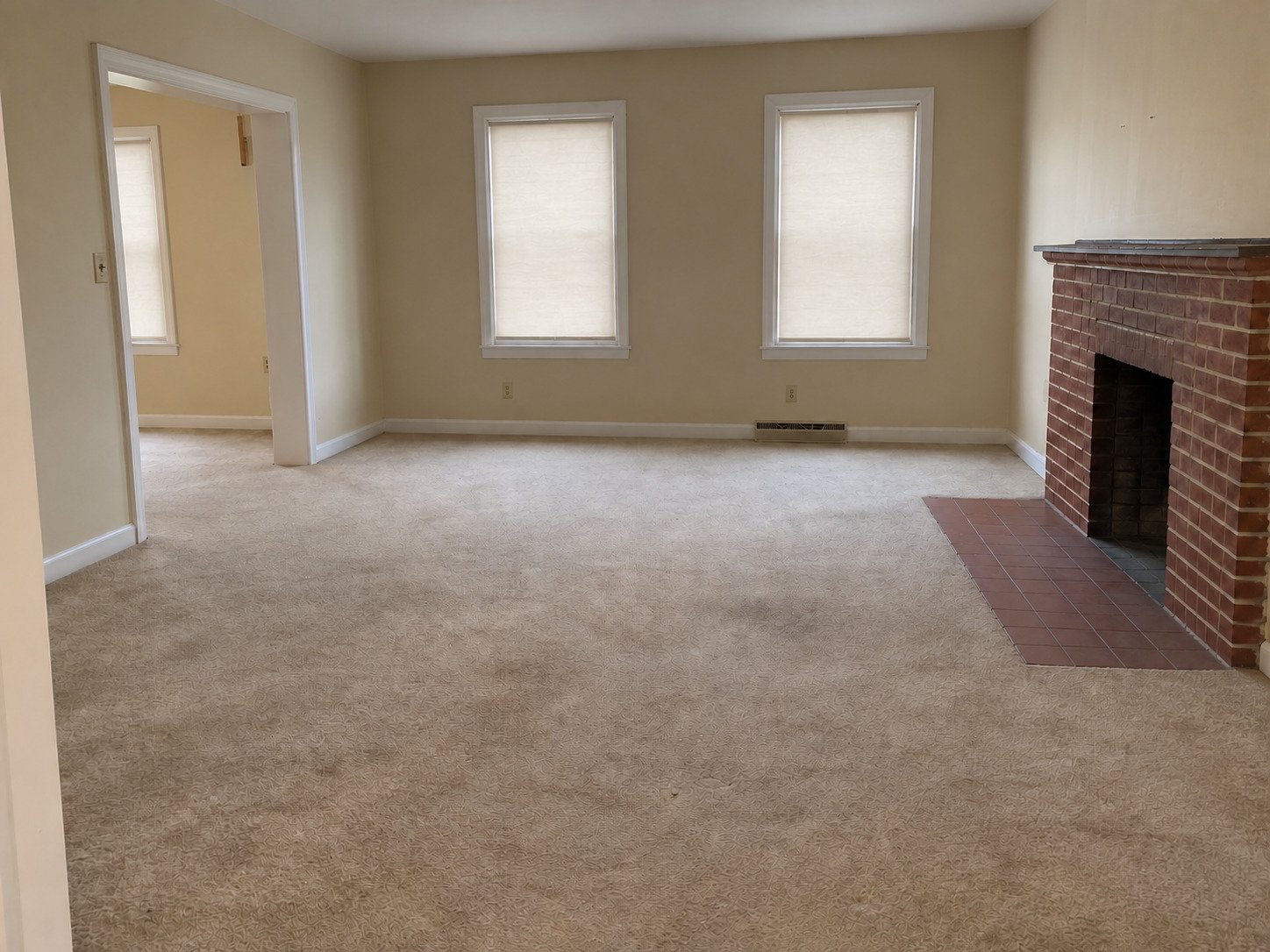 The same estate living room cleared of contents, with worn carpet and brick fireplace retained.