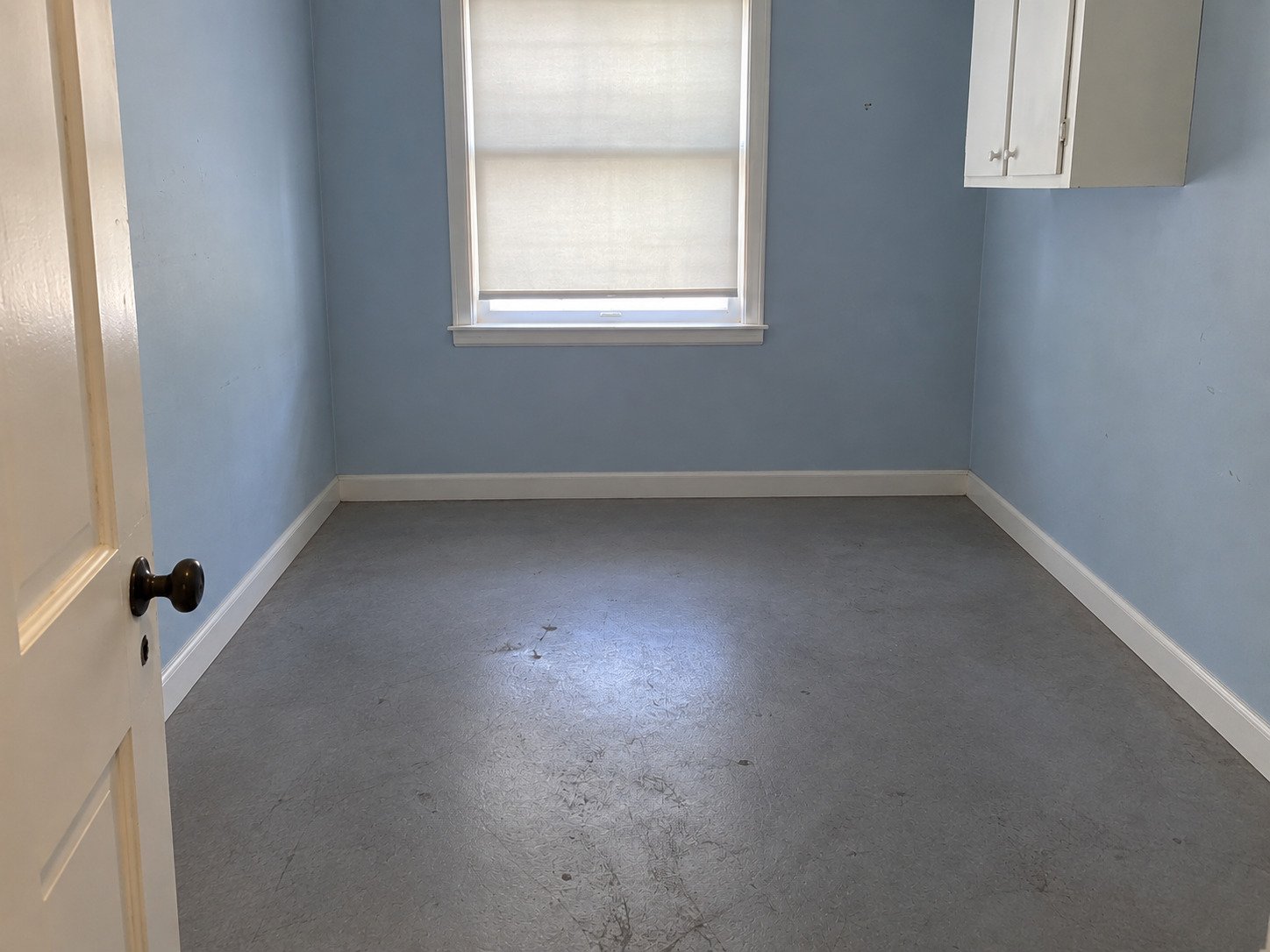 The same blue storage room after contents removal, retaining its fixed wall cupboard and scuffed gray floor.