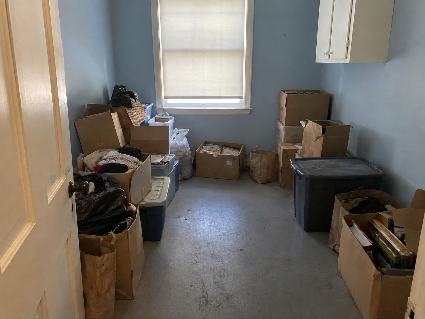 Blue storage room with boxes, totes and bagged belongings before estate cleanout.