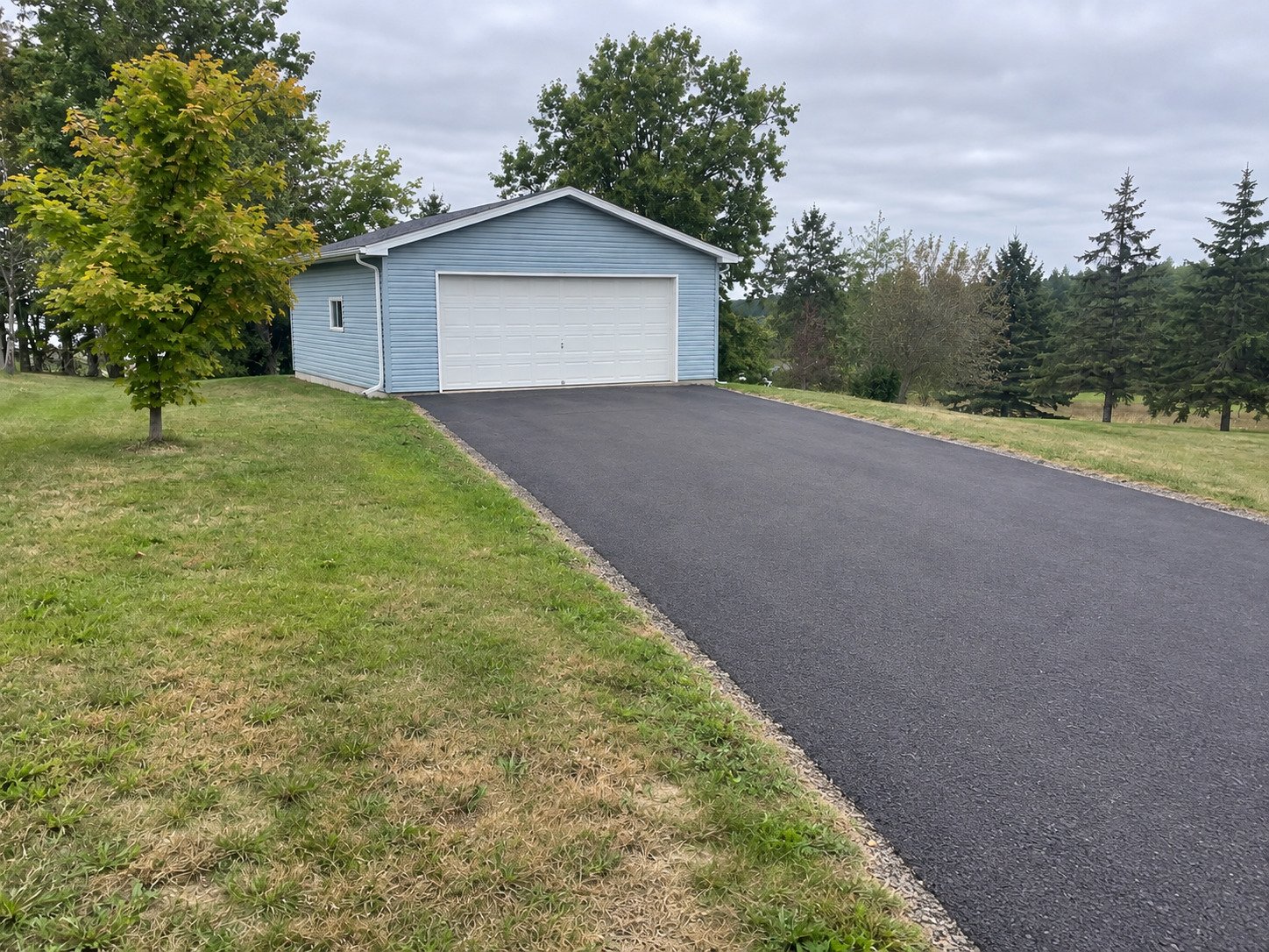 The same detached garage with a new dark asphalt driveway and tidy edges.