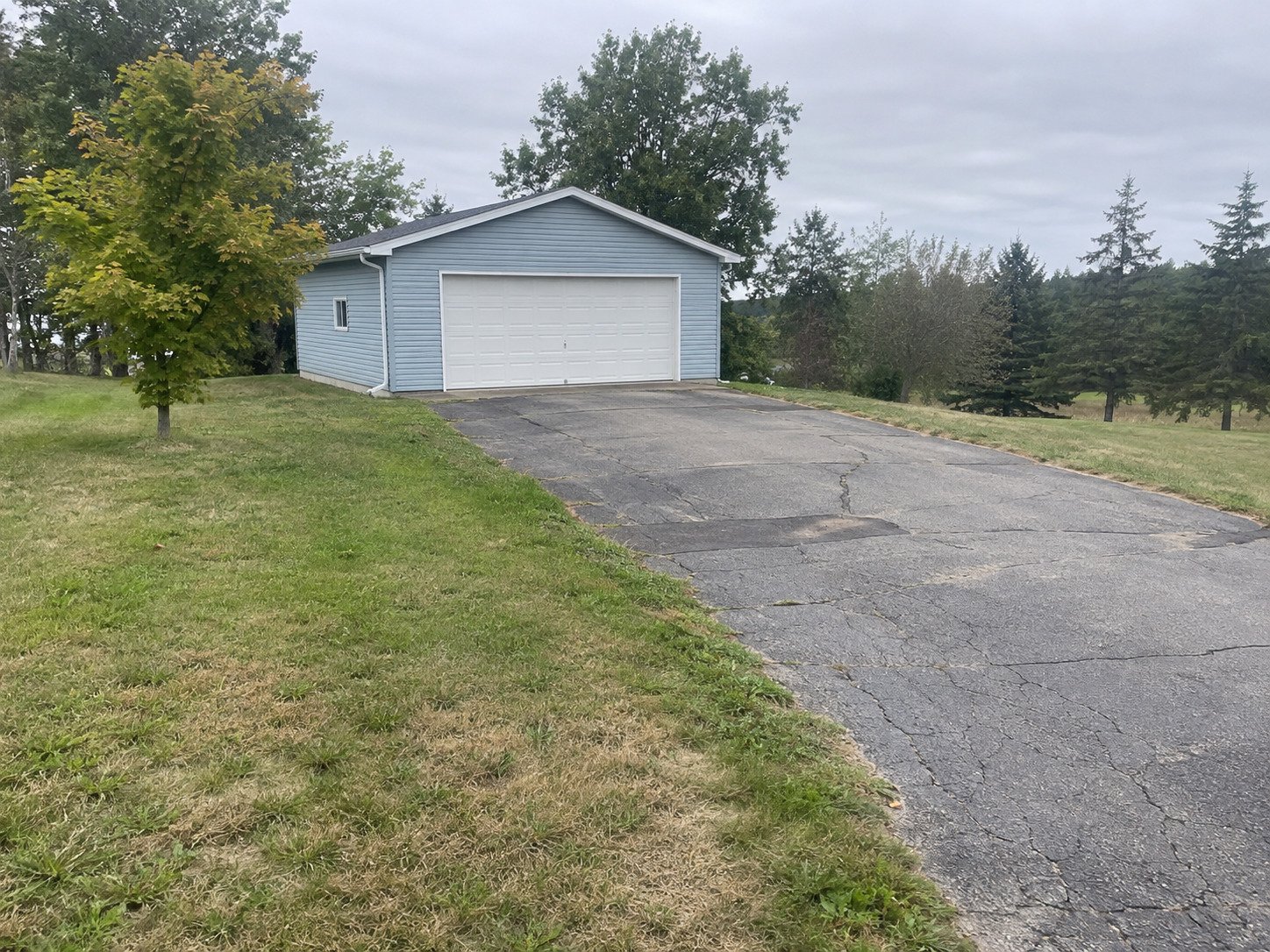 Cracked driveway approaching a blue detached garage before paving.