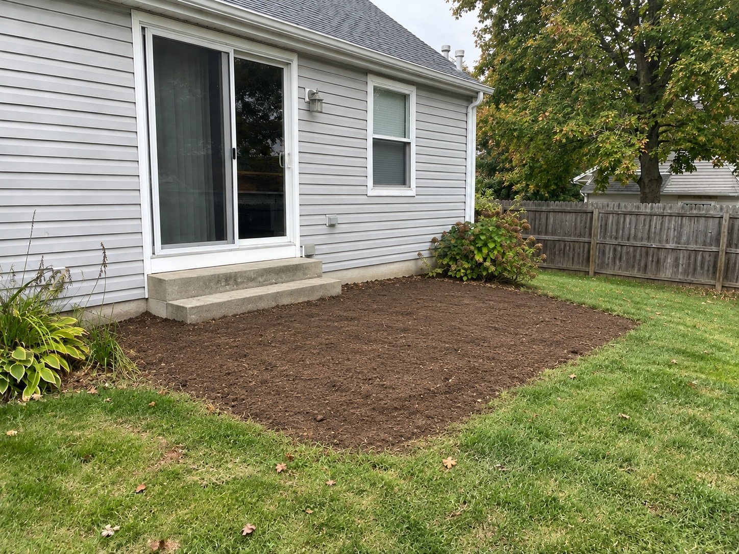 The same house after the attached wooden deck is removed, with the footprint cleared and concrete access steps retained.