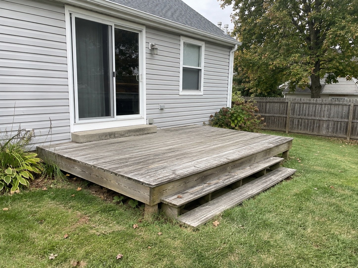 Weathered deck attached to a house and serving its rear patio door before removal.