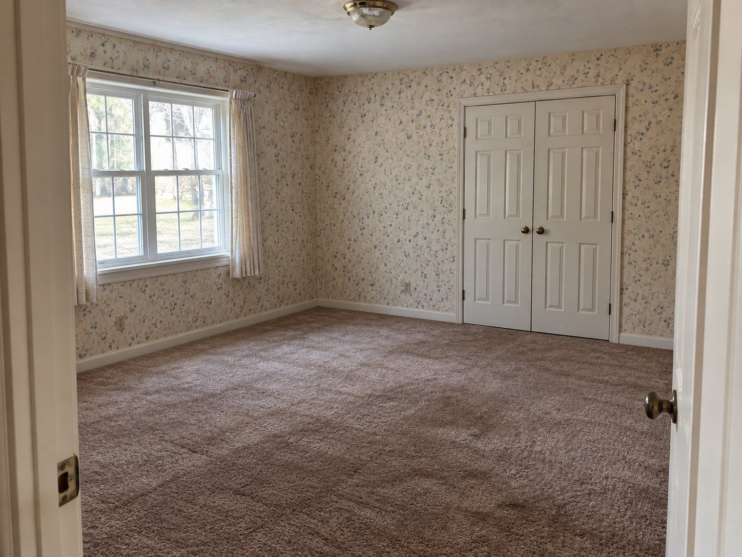 The same spare bedroom cleared, retaining worn brown carpet and floral wallpaper.