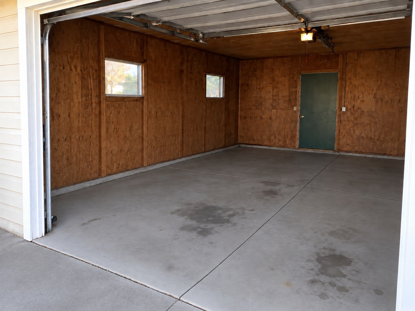 The same garage cleared of stored belongings, retaining old concrete stains and installed door hardware.