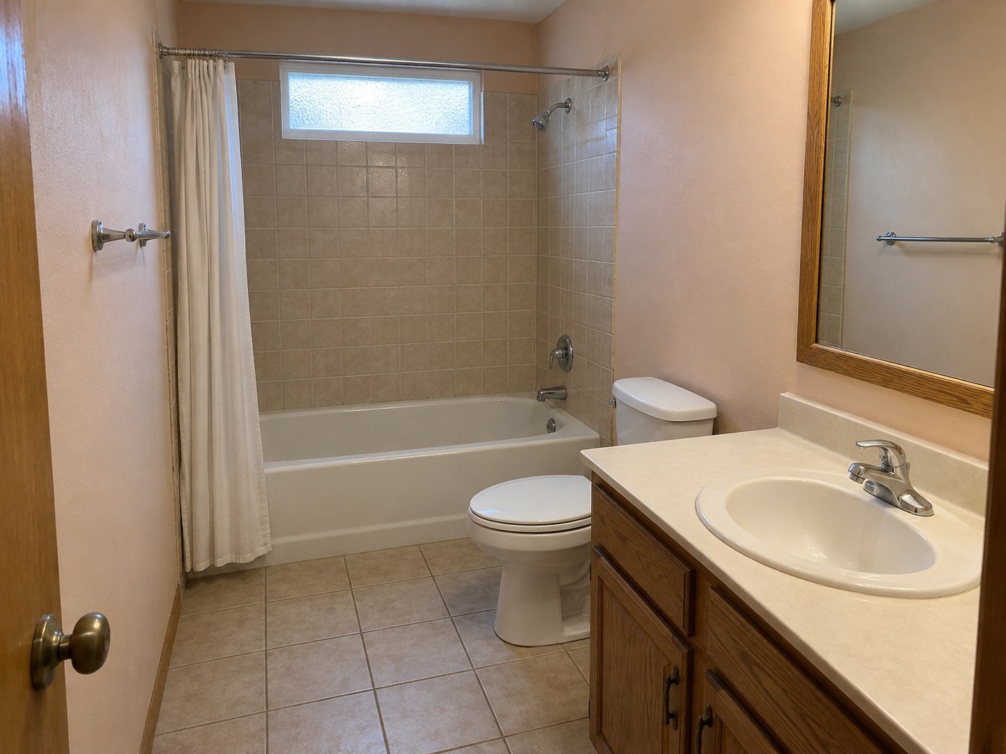 Representative dated bathroom with beige tile and an oak vanity before a finish refresh.