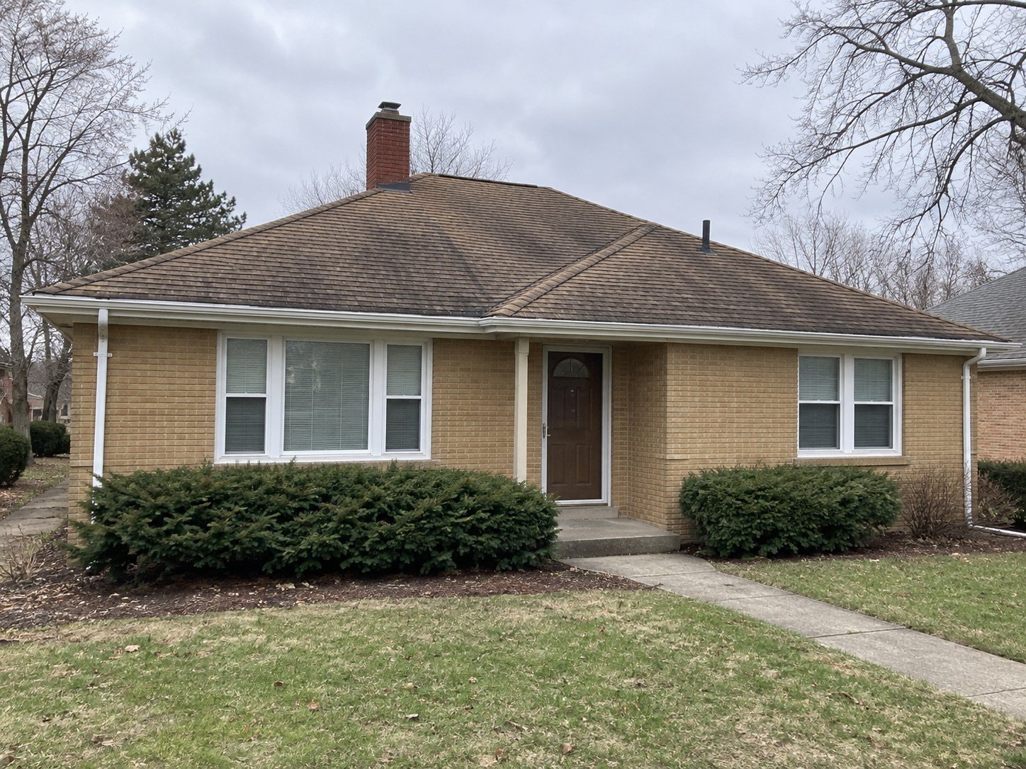 Representative aging brown shingle roof on a tan brick home before replacement.