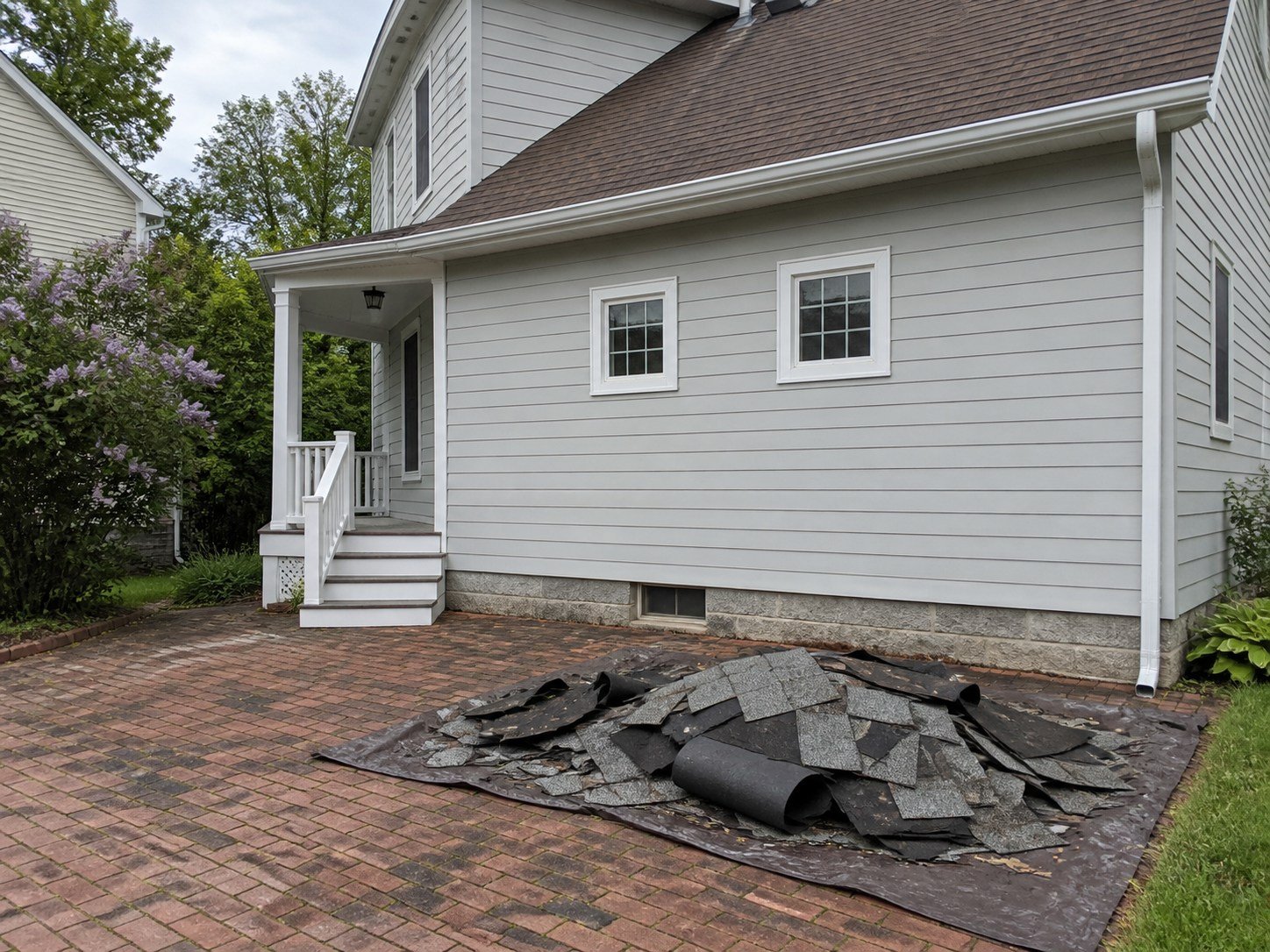 Roof tear-off shingles and felt staged on a tarp before debris hauling.