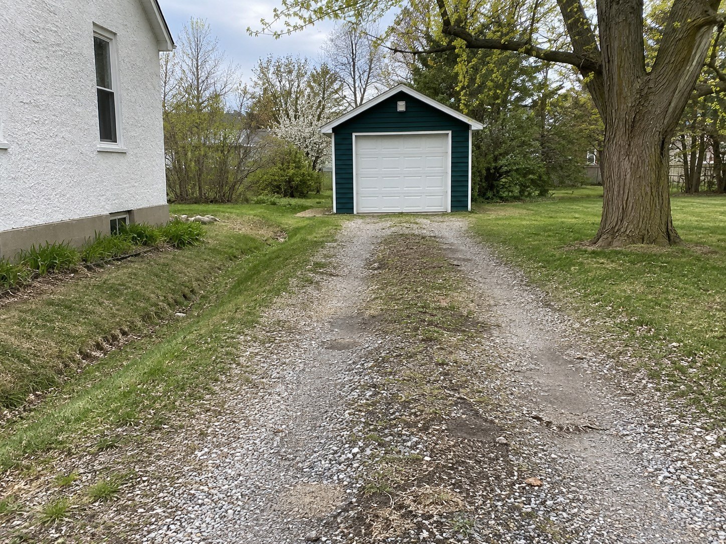 Worn gravel driveway with shallow wheel ruts leading to a detached green garage.