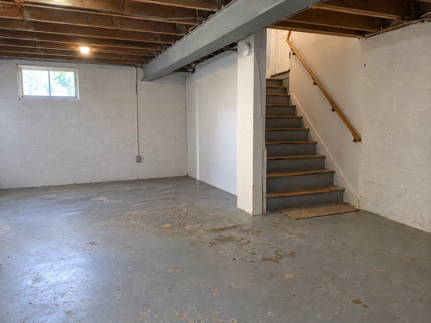 The same basement cleared while retaining the stairs, handrail, structural beam and worn painted concrete.