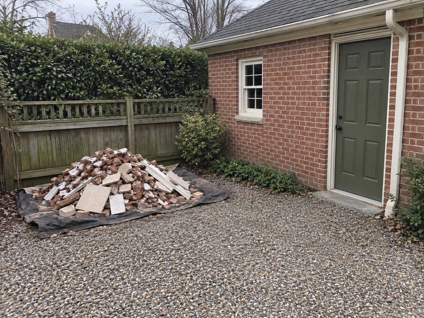 Masonry and trim debris awaiting hauling beside an intact brick garage.