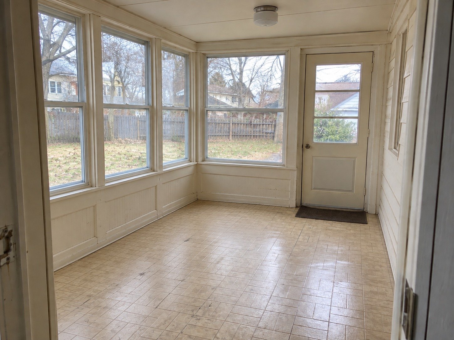 The same sunporch cleared of stored contents, retaining its worn floor, windows and exterior door.