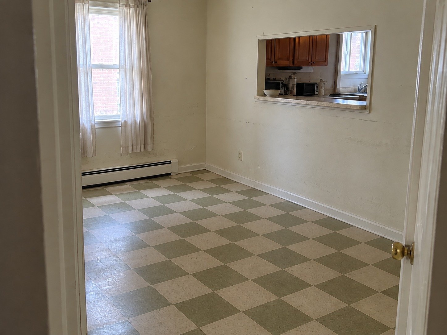 The same dining nook empty after contents removal, retaining its old checker floor and existing kitchen pass-through.