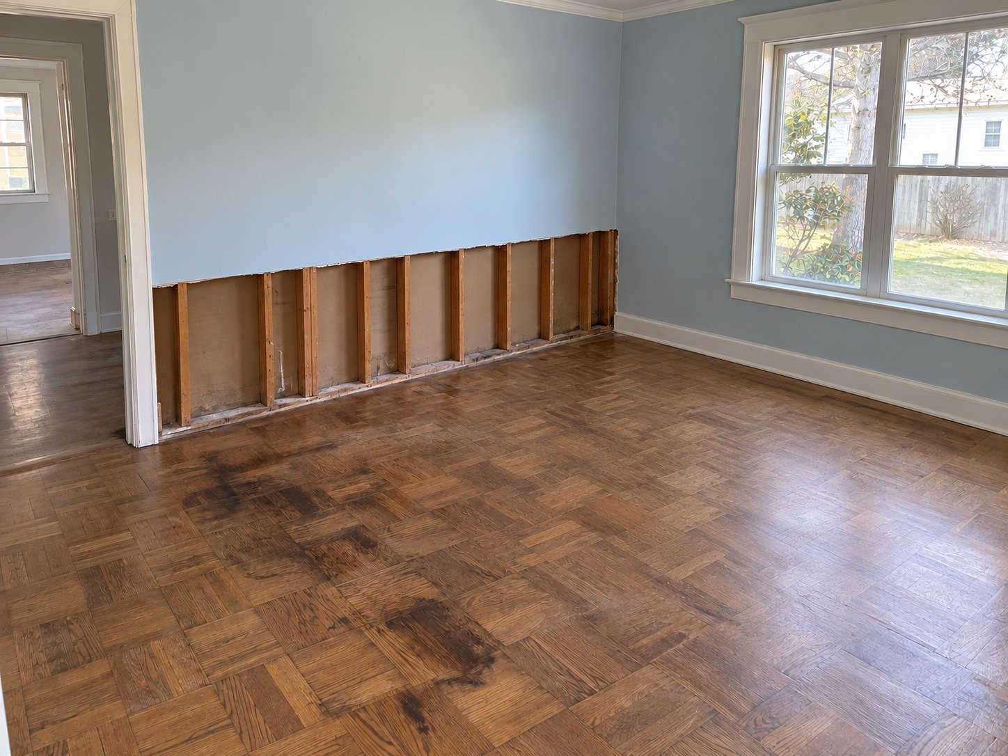 The same room after debris removal, with stained parquet and open walls still awaiting restoration.