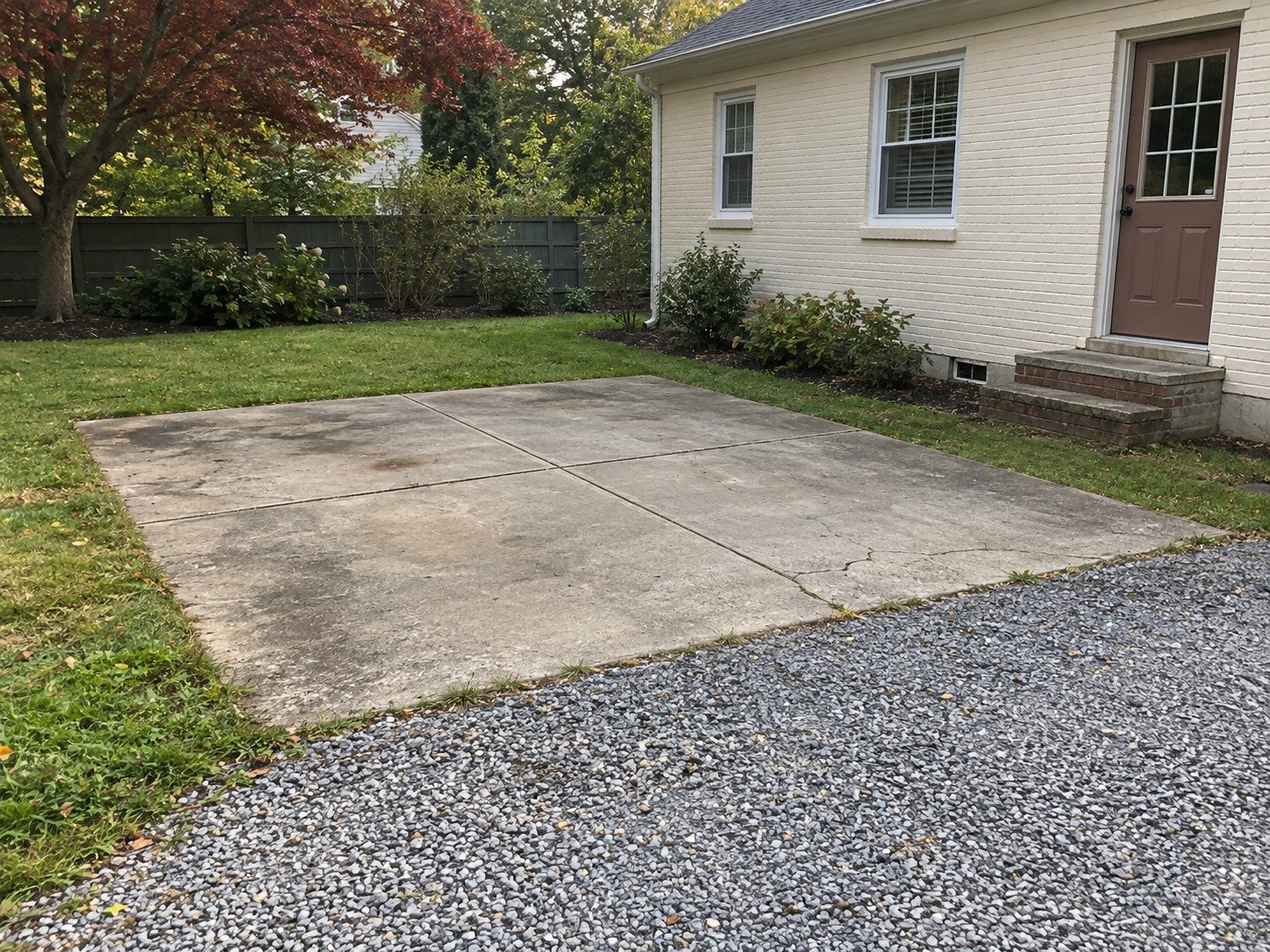Existing obsolete concrete parking pad beside a gravel drive before removal.