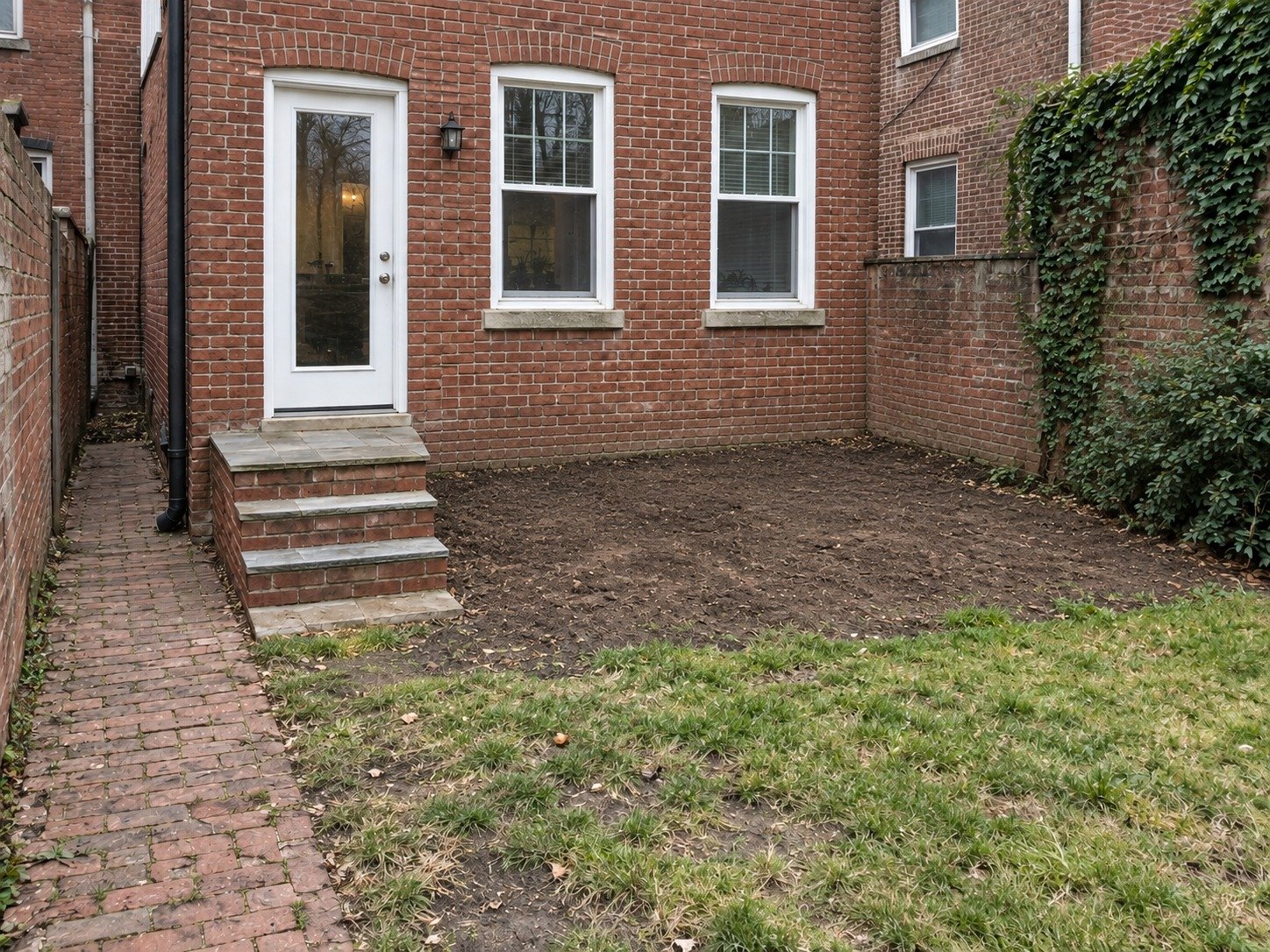 The same brick rowhouse after deck removal, with the original back-door steps and garden access retained.