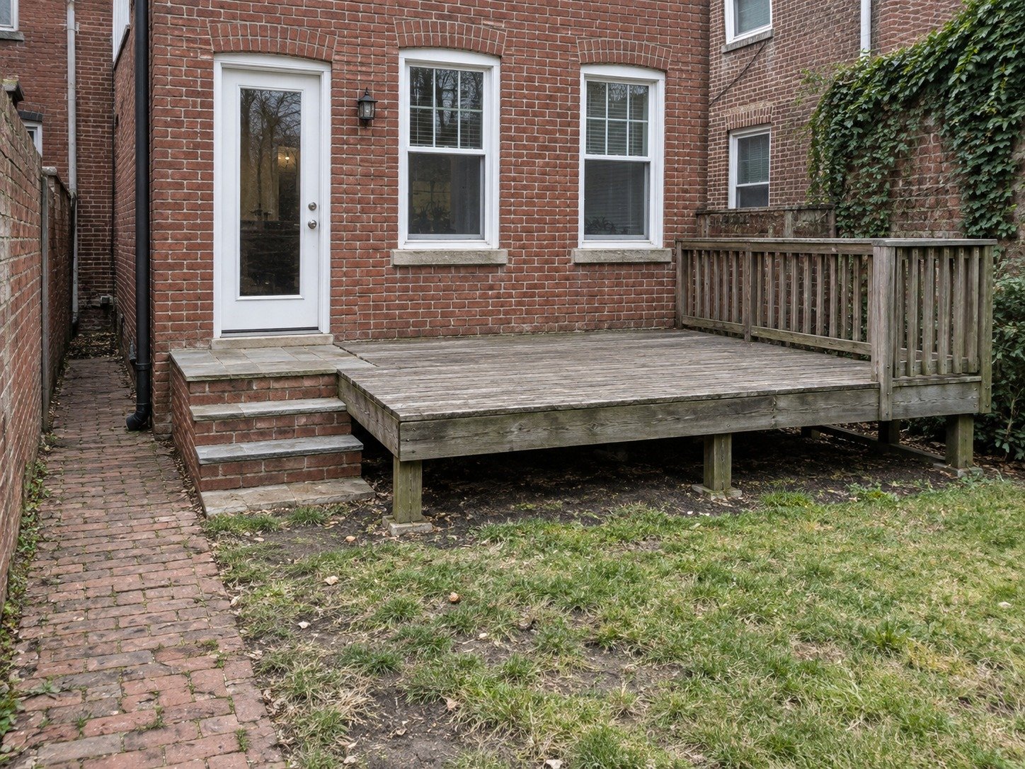 Weathered house-connected wood deck beside the back-door masonry steps at a brick rowhouse before removal.