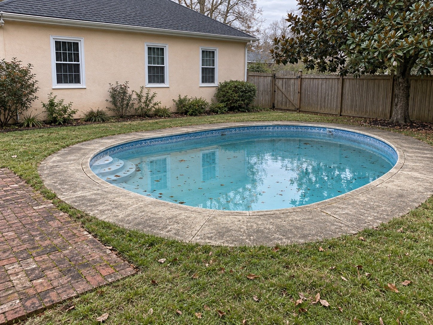 Oval in-ground pool with aged concrete surround before removal from an enclosed backyard.