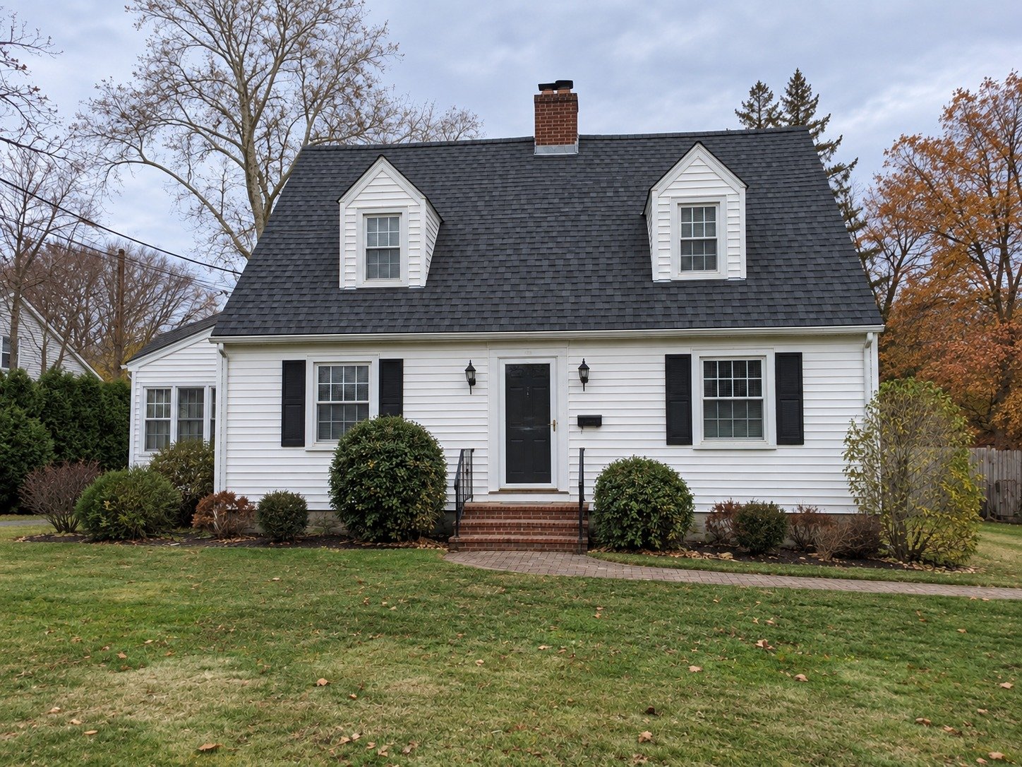 Cape with a renewed charcoal shingle roof, retaining its dormers and brick chimney.