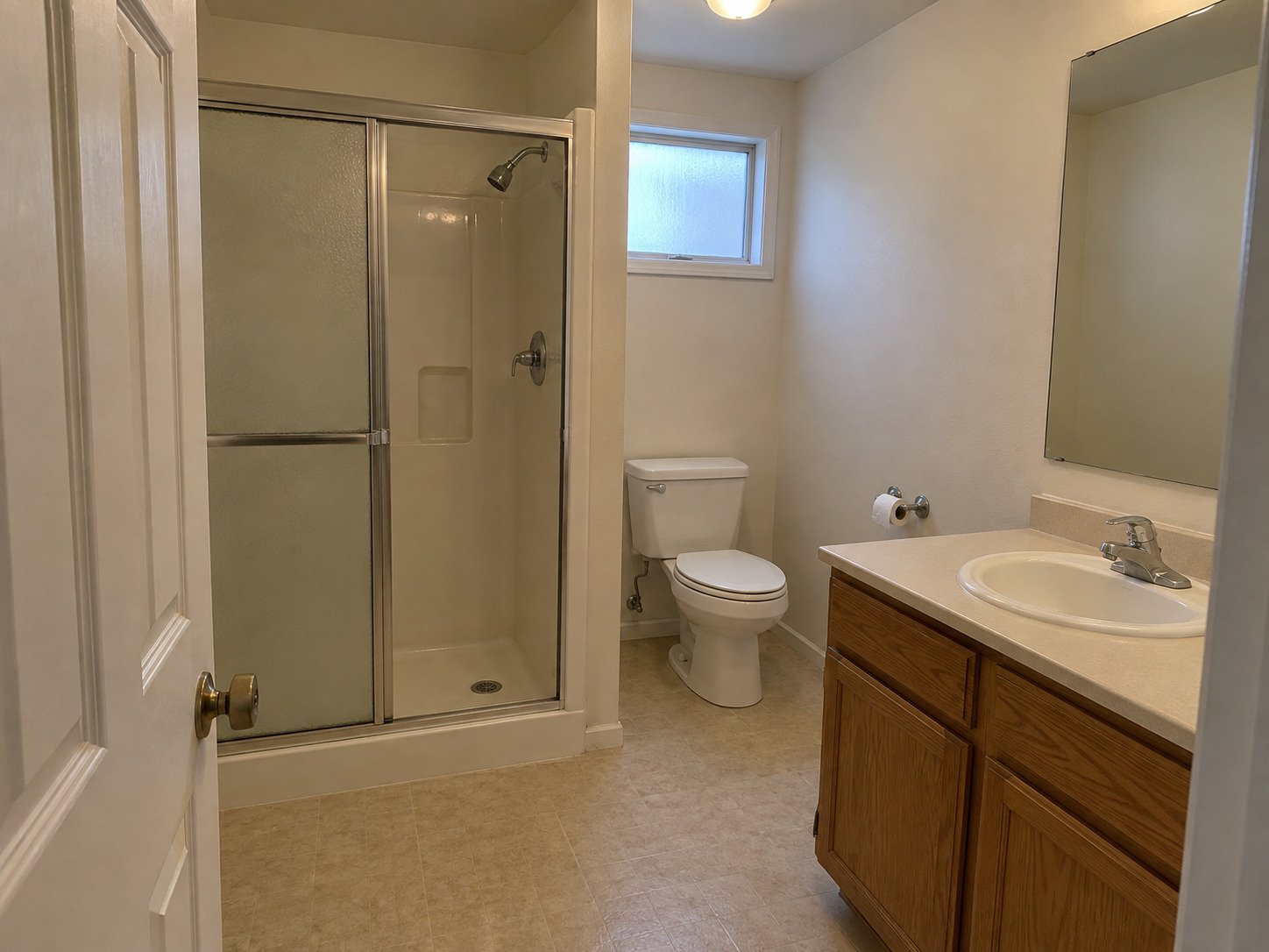 Compact bathroom with an older fiberglass shower and oak vanity before remodeling.