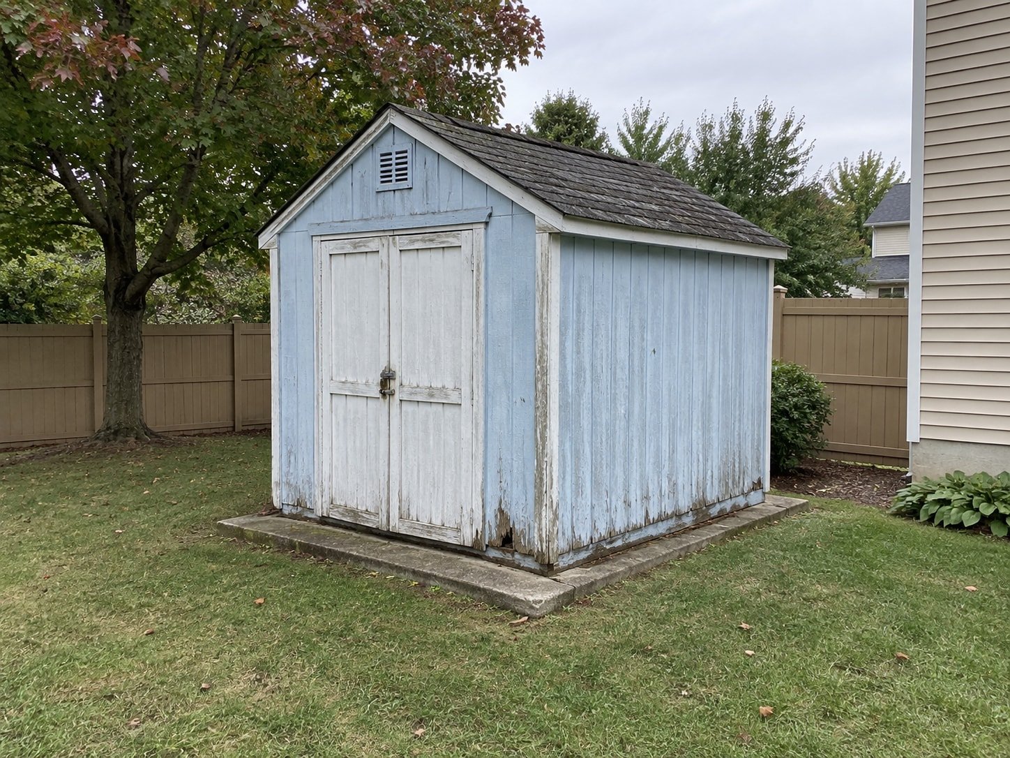 Weathered blue wood shed on a concrete pad before removal.