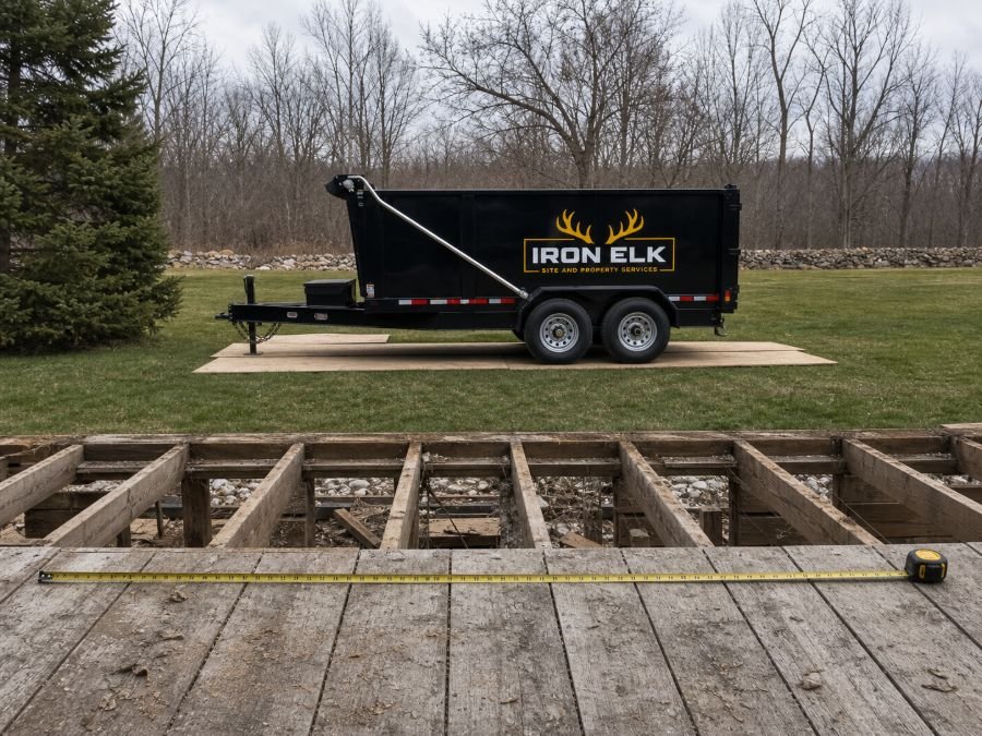 A tape measure stretched across a stripped deck frame, the empty trailer waiting on the lawn.