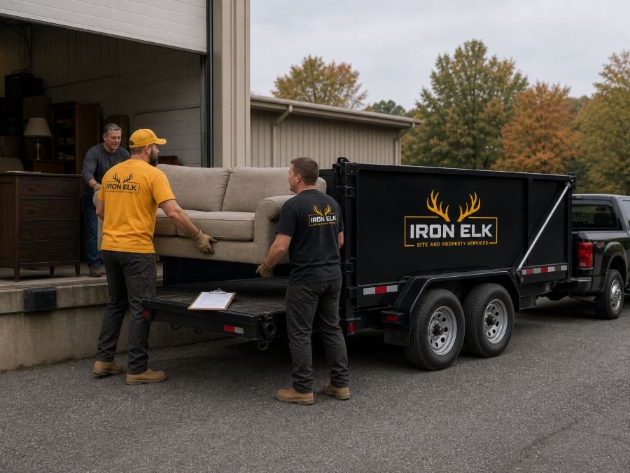Two workers carrying a couch out of a garage to the waiting trailer.