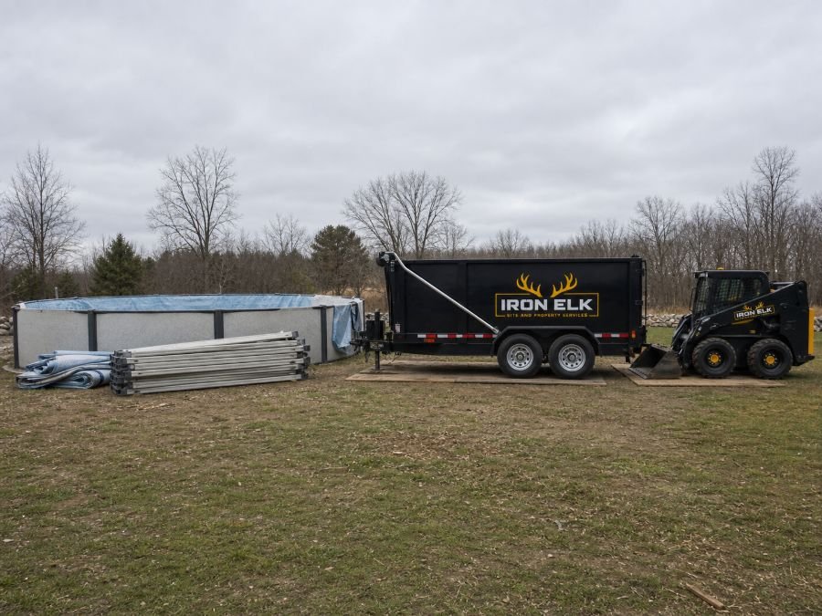A drained above-ground pool with a compact loader and trailer standing by.