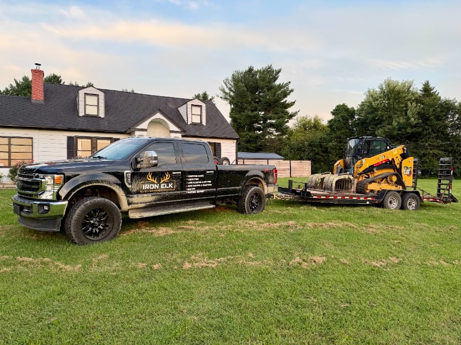 Iron Elk pickup truck towing an equipment trailer carrying a skid-steer loader.