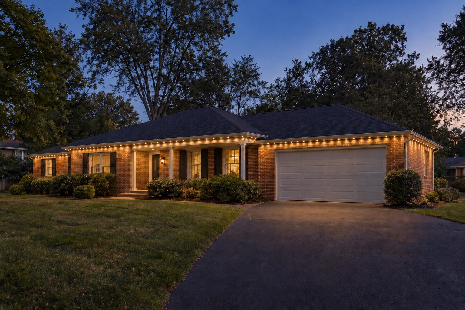 Single-story brick ranch after dark, with small warm-white permanent lights beneath its visible roofline and entrance canopy.