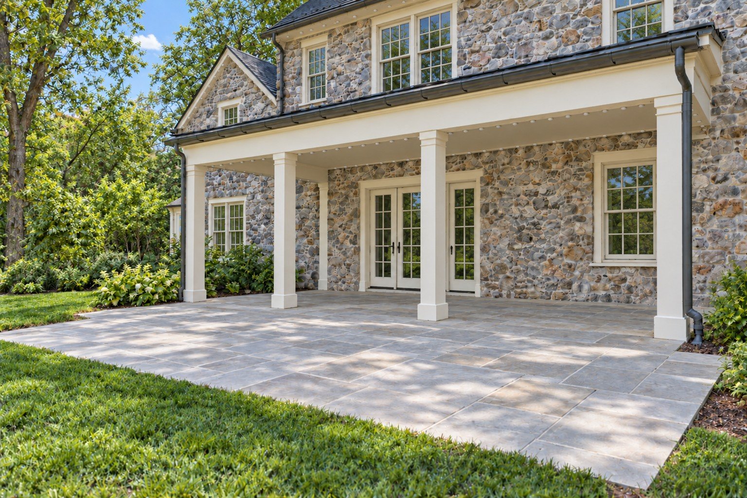 Daylight view of the same stone-home covered patio, with all perimeter, upper-eave and gable-edge lenses present and switched off.