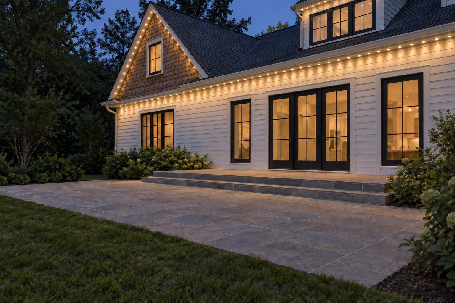 Rear exterior with warm-white permanent lights along the cedar gable, dormer and lower eaves.