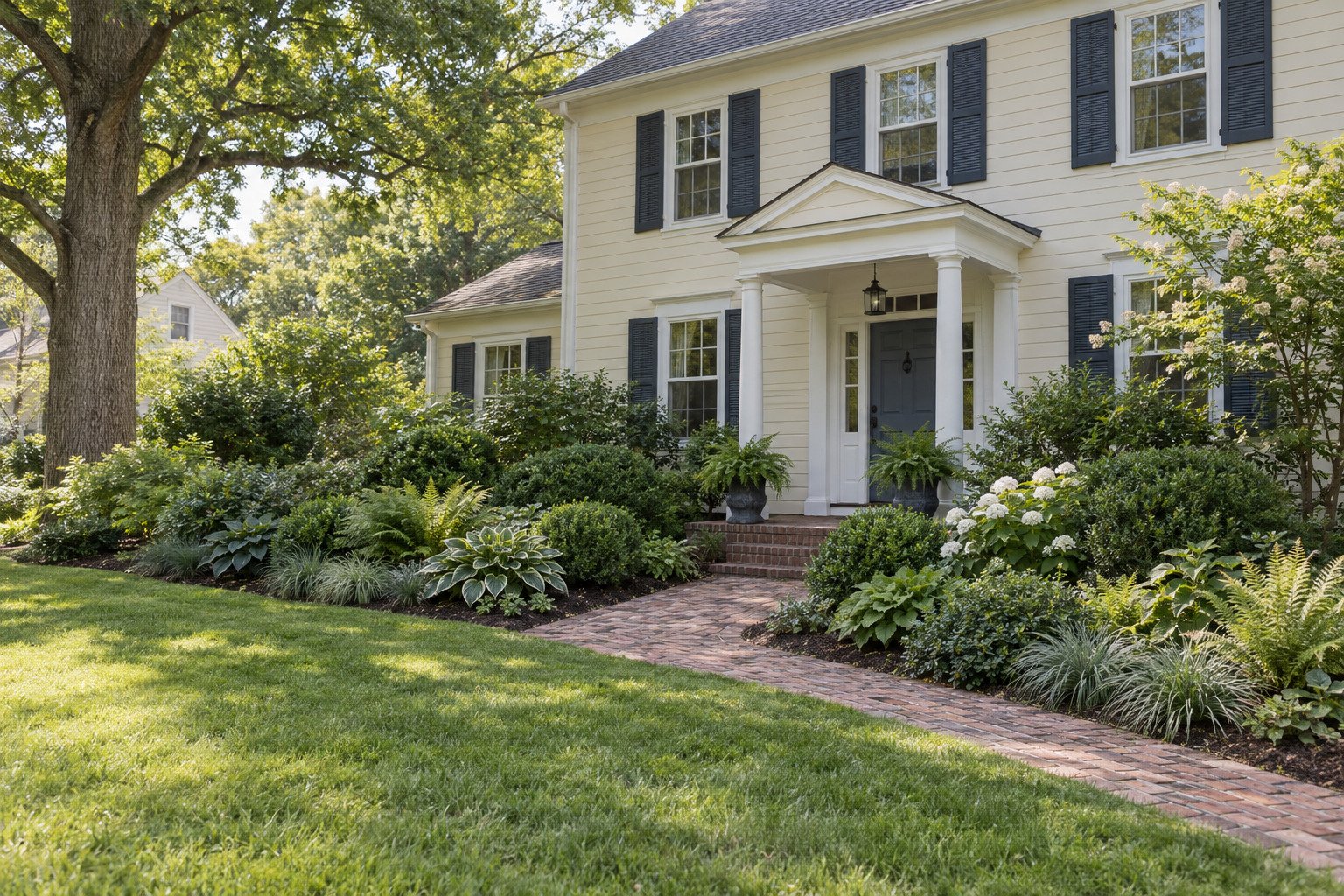 After view of richly layered shrubs, ferns, grasses and perennial foliage at the same colonial home.