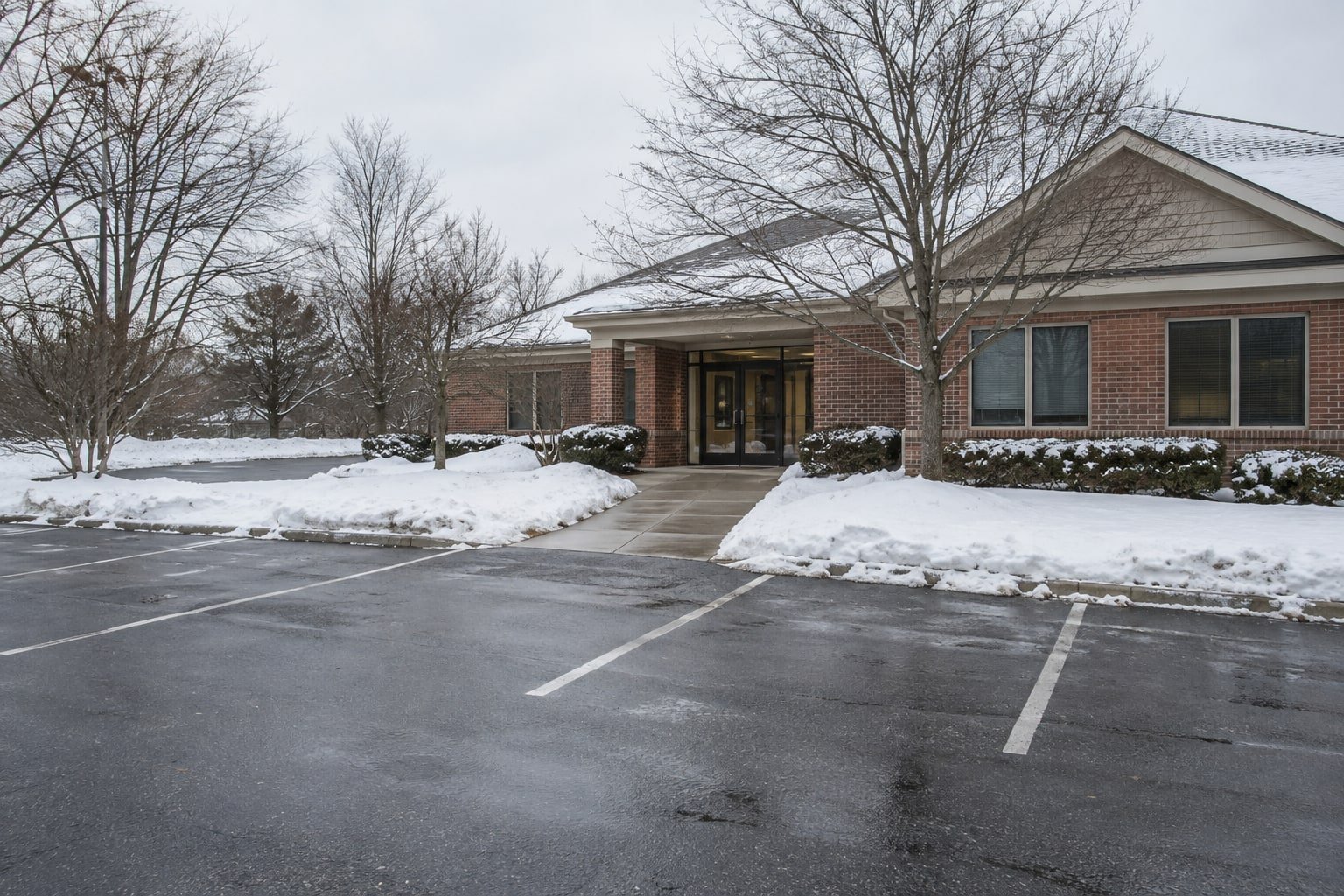 Plowed parking lot and cleared entrance walkway at a brick office, snow banked on the lawn.