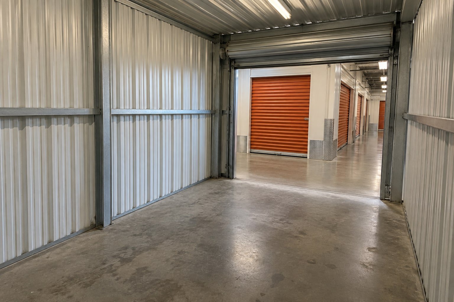 Emptied indoor self-storage unit with roll-up doors along the corridor beyond.